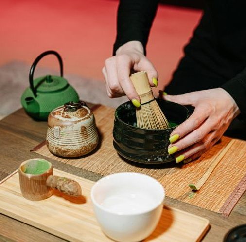 Close-up of hands preparing matcha in a traditional Japanese tea ceremony with utensils.